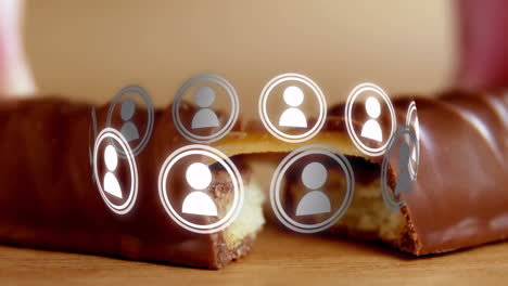 Floating digital user icons over chocolate bar on wooden surface in animation