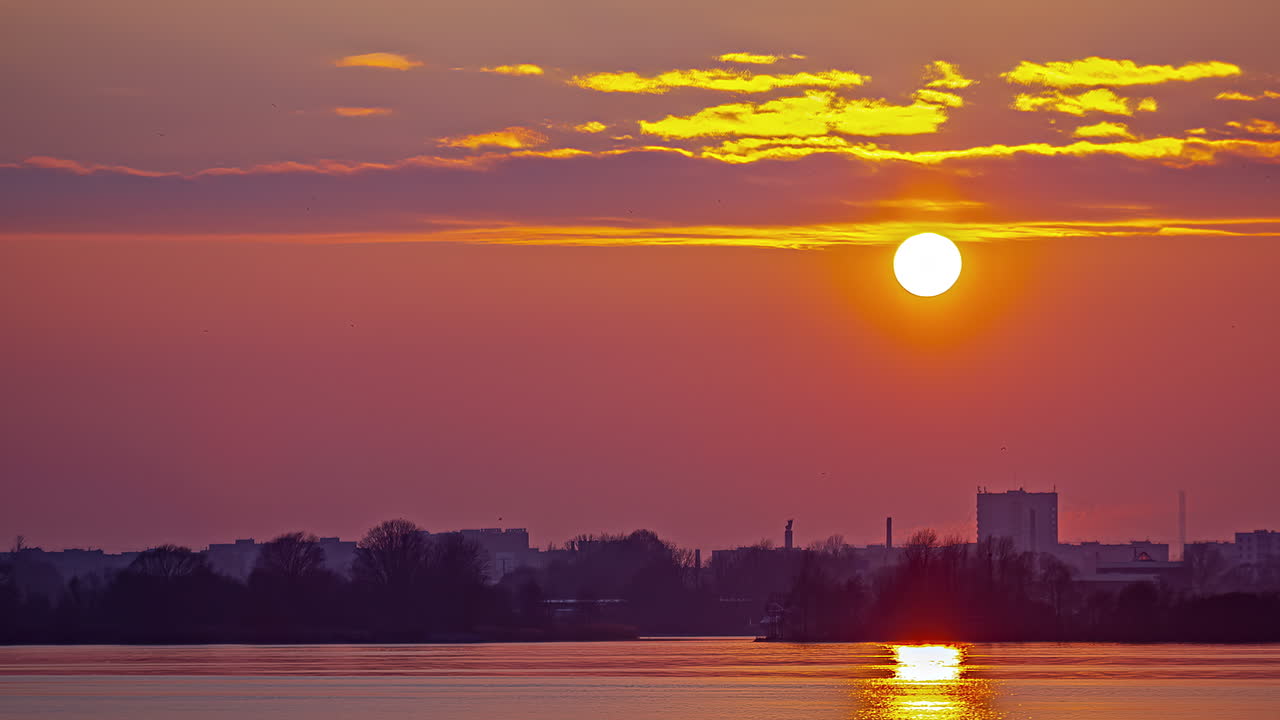 Auringonlaskun aikaviivekuvaus satamakaupungista, kultaisen hehkun heijastuessa merestä