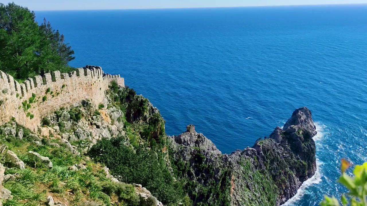 Vista panoramica costiera delle mura della fortezza storica del Castello di Alanya che si ergono su aspre scogliere rocciose, affacciate sul profondo Mar Mediterraneo blu ad Antalya, Turchia.