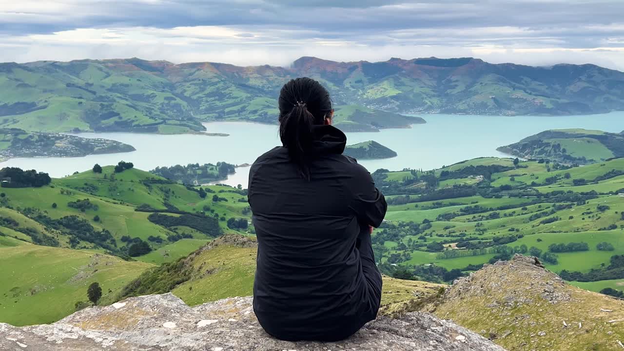 Woman enjoys serene view from Montgomery Peak on Akaroa Peninsula, New Zealand