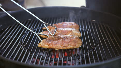 turning or flipping spiced chicken breasts grilling on the barbecue - slow motion