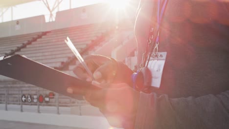 Midsection-of-african-american-male-coach-time-cheking-and-making-notes