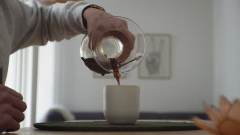 Casual-Millenial-pouring-hand-brewed-coffee-into-caramic-cup-in-his-living-room