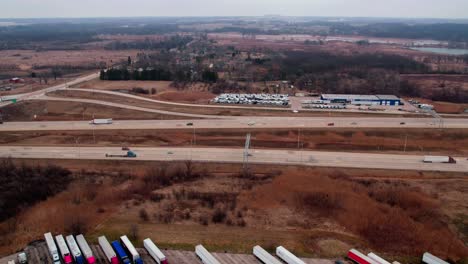 Timelapse-of-I-94-highway-above-a-truck-stop-with-semi-trucks-aligned-and-parked