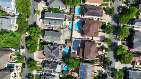 Aerial-top-down-shot-showing-american-neighborhood-with-private-swimming-pool-and-solar-panels-on-roof---circling-drone-flight