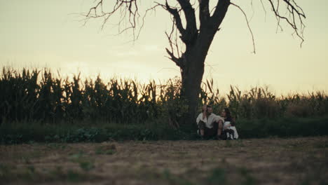 couple sitting under a bare tree in a field at sunset