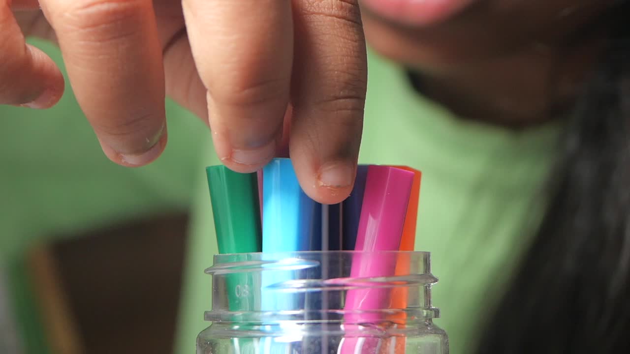 Child putting colorful markers in a jar