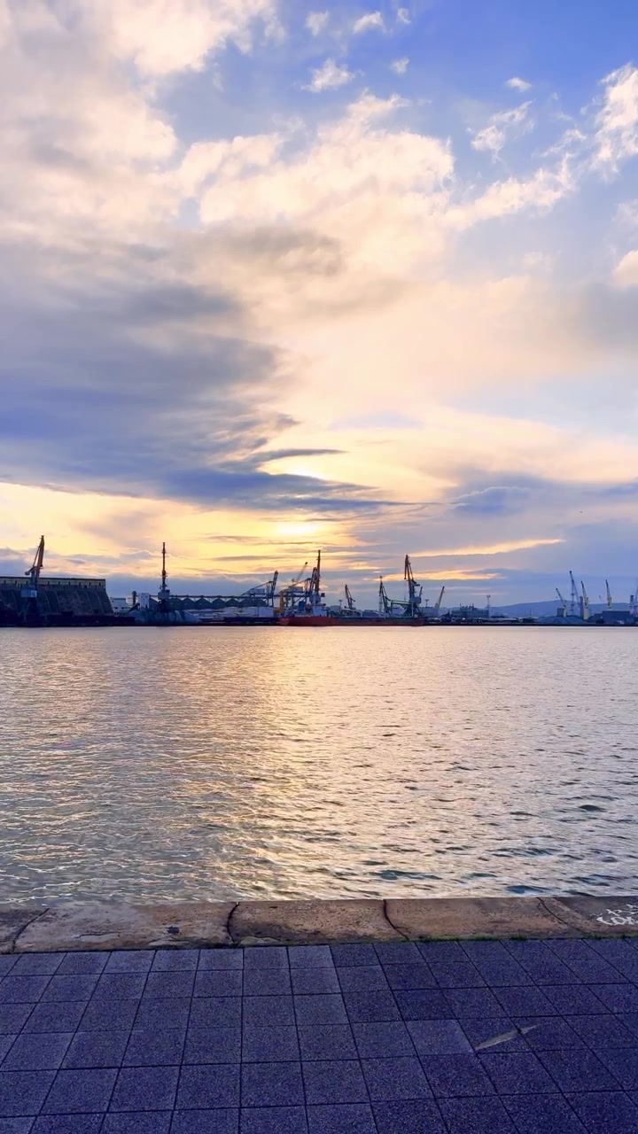 Harbor sunset with cranes. The sun sets over the harbor, casting a warm light on the water and cranes in the distance against the sky.