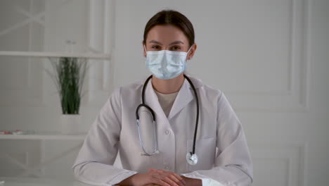 young pretty female doctor with a face mask looks at camera and smiles at the office