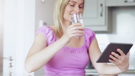 Blonde-drinking-glass-of-water-using-tablet-