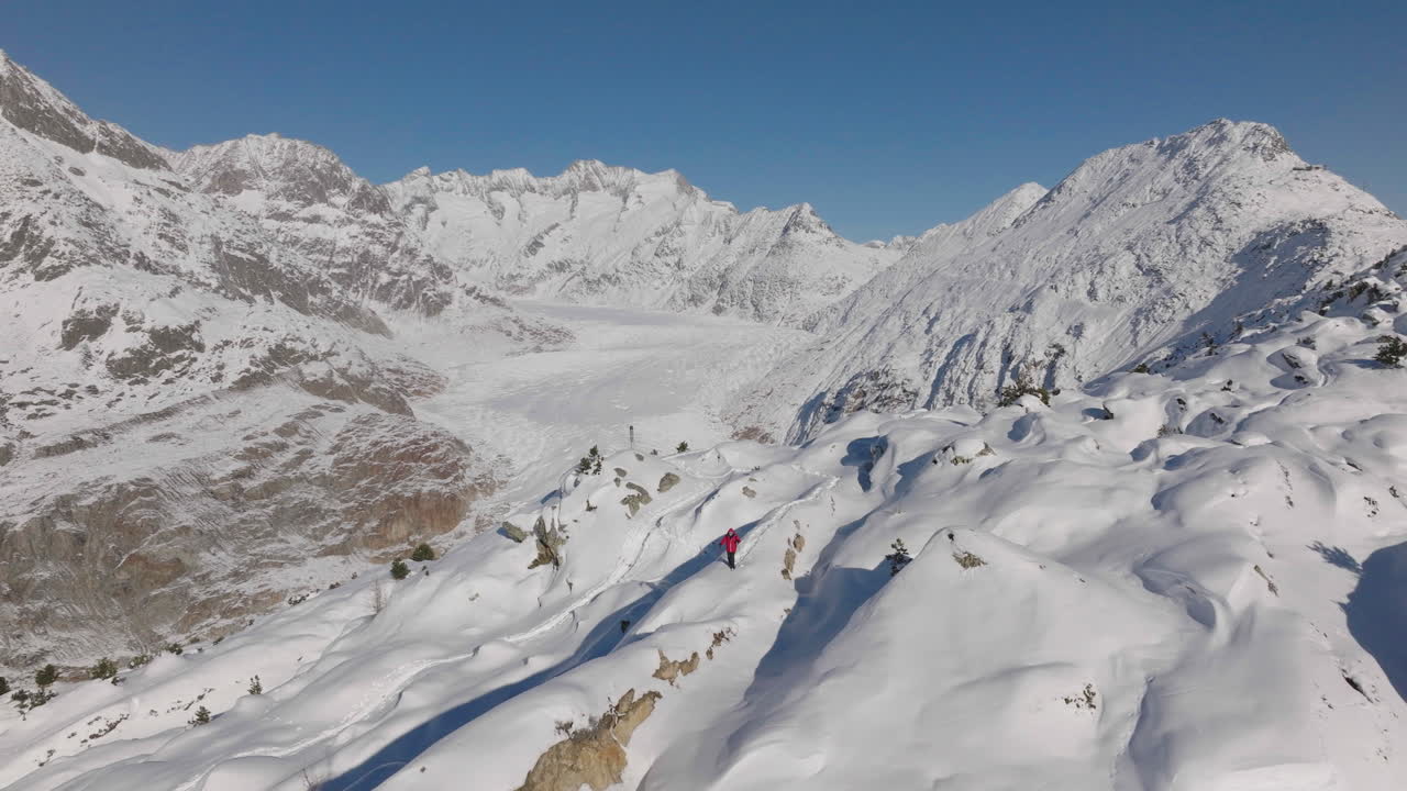 toma aérea en suiza con una persona caminando con raquetas de nieve en un día soleado con un glaciar detrás