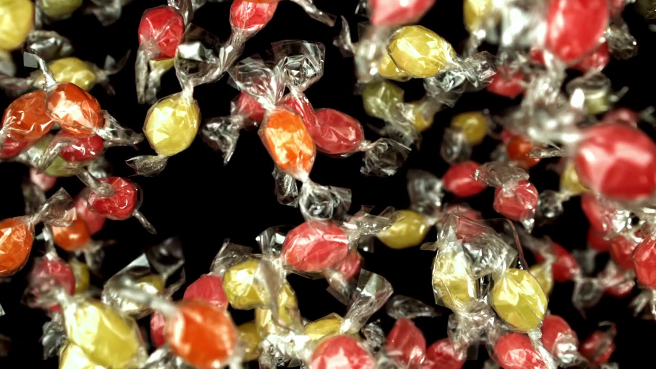 Caramelle colorate incartate che cadono al rallentatore su sfondo nero