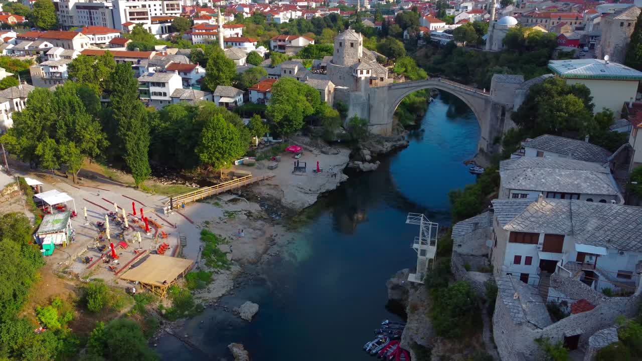 Aerial view overlooking iconic Mostar Bridge, Neretva river and small cove on wonderuful clear summer's morning with almost no people