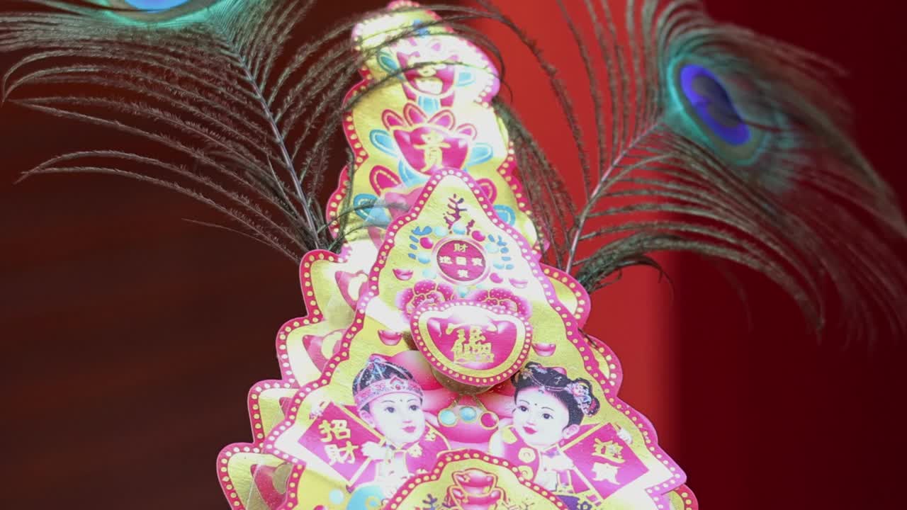 Plumas de pavão vibrantes balançam suavemente atrás de uma decoração de papel colorida e ornamentada contra um plano de fundo vermelho