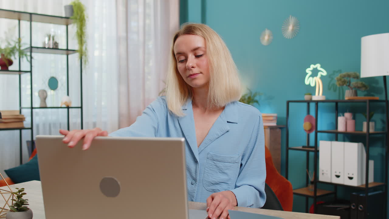 Ung forretningskvinde på hjemmekontoret, der sidder ved skrivebordet og åbner bærbar computer, begynder at arbejde og sender beskeder