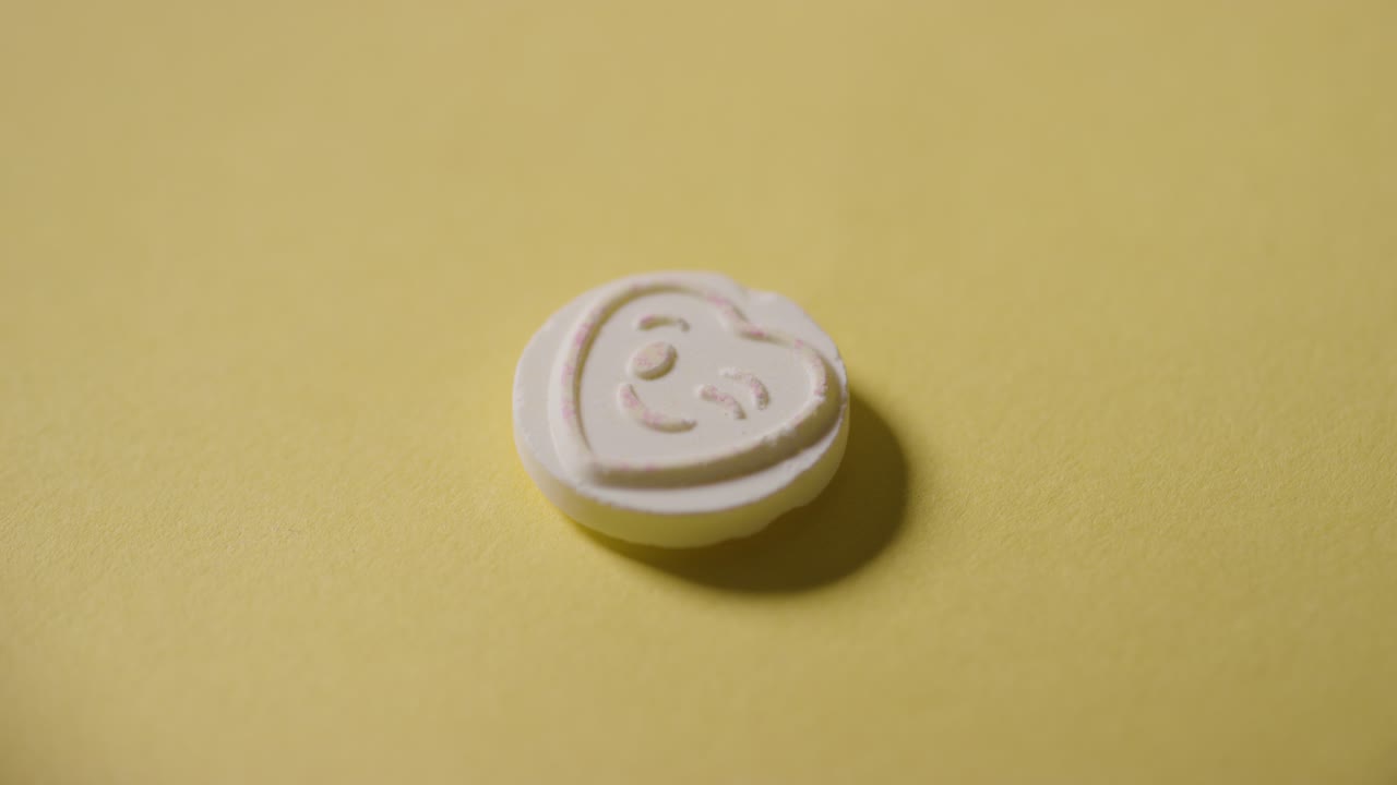 노란색 배경에 윙크하는 이모티콘으로 하트 사탕을 손에 들고