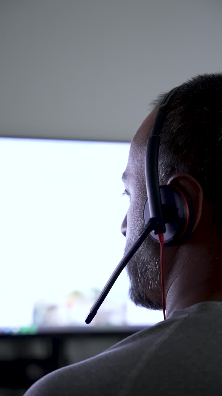 Primo piano da dietro di un uomo che indossa una cuffia, che guarda uno schermo di computer luminoso con contenuto sfocato, che rappresenta lavoro online, comunicazione o collaborazione virtuale.