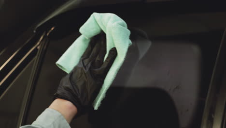 ingeniero con guantes negros y usando un paño de microfibra verde para limpiar el espejo de la ventana del coche