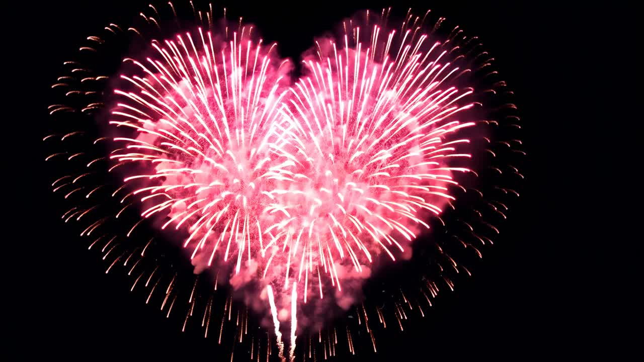 Aerial view of vibrant pink heart-shaped fireworks against a dark sky, capturing a festive
