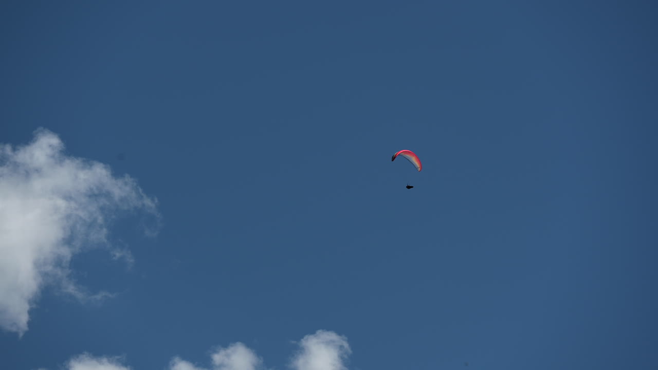 un paracaídas colorido vuela en un cielo azul con algunas nubes sobre los alpes suizos durante el mediodía