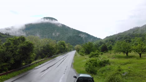 汽車在鄉村地區的潮<unk>道路上行駛,背景是霧<unk>的山丘 - 空中