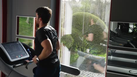 athletic male in dark sportswear run on treadmill, reflection on gym window