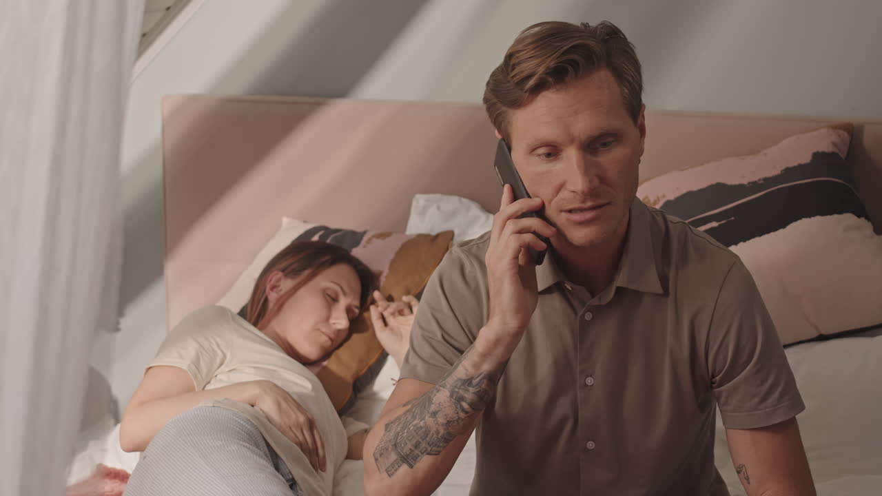 Mann som snakker i telefonen mens kvinne sover