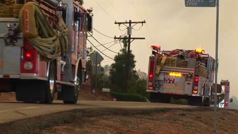 medium shot of fire trucks racing down a street toward a wildfire