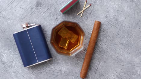 Glass-of-whiskey-with-ice--big-cuban-cigar--matches-and-hip-flask