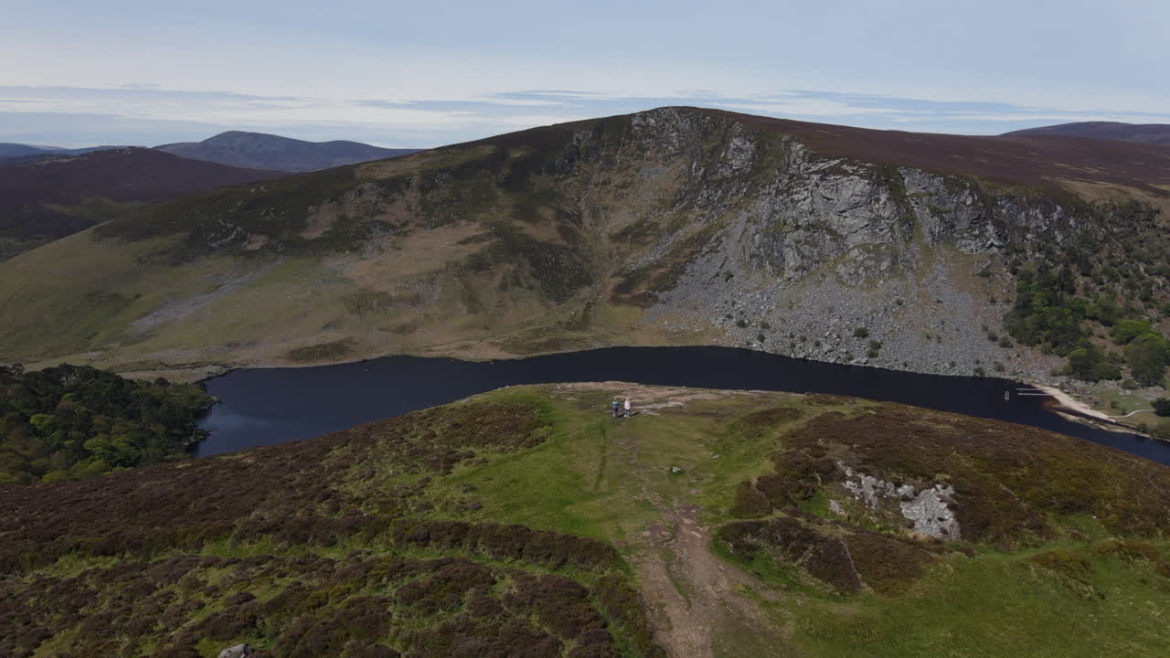dos personas caminando hacia el borde de lough tay en wicklow, en irlanda