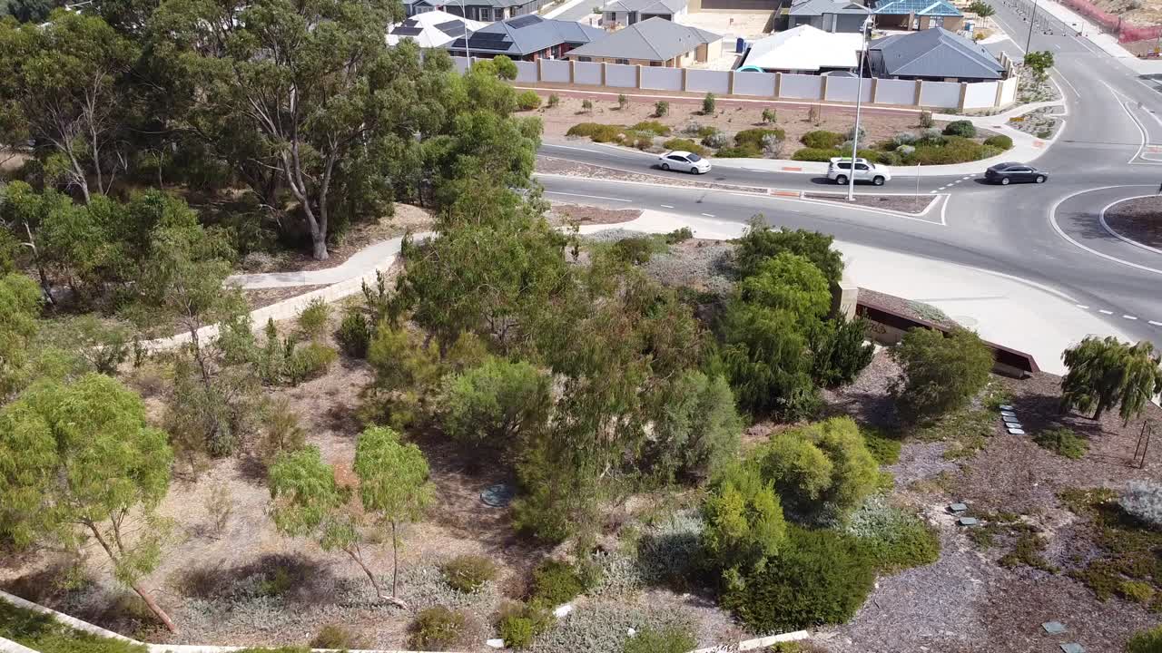 Vehicles, moving trees and buildings above an Australian city, aerial