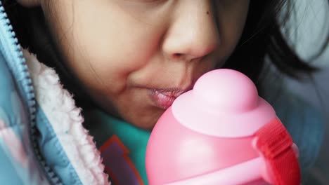 niño bebiendo de una botella de agua rosa