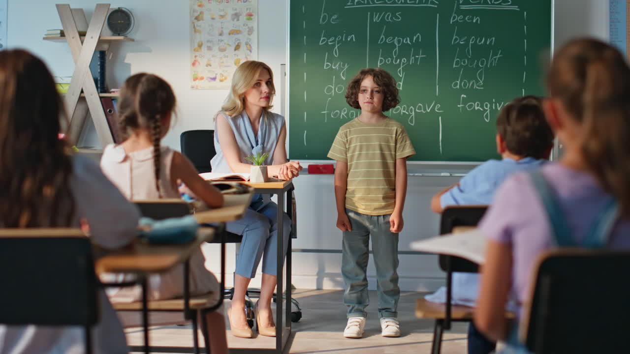 School boy speaking class answering lesson near blackboard. Woman teacher asking