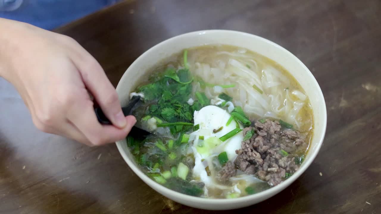 Person eating pho beef with spoon