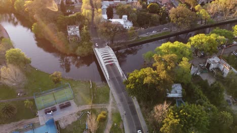 Toma-Aérea-De-Pájaros-De-Autos-Cruzando-El-Puente-Sobre-El-Arroyo-En-Tigre-Cerca-De-Buenos-Aires-Durante-La-Hermosa-Luz-Del-Atardecer