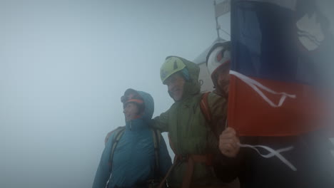 Happy-hikers-with-helmets-posing-in-front-of-Aljaž-Tower-and-wawing-Slovenian-flag