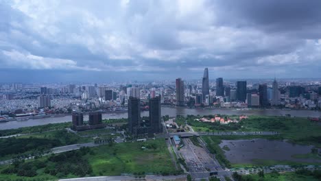 Aerial-fly-in-to-Ho-Chi-Minh-City,-Vietnam,-skyline-during-day-time-with-dramatic-highlights-and-shadows,-boats-on-Saigon-river-and-road-traffic-new-residential-and-commercial-development