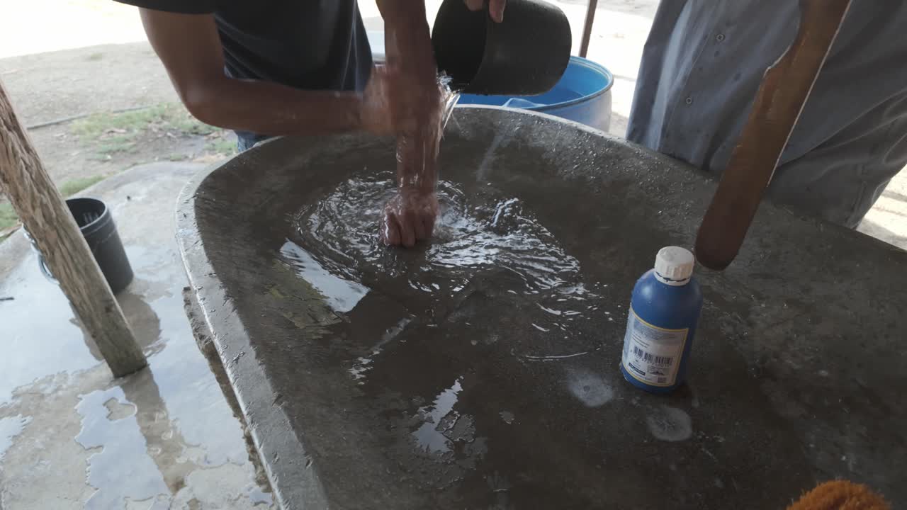 Man washing hands in a concrete basin with a wooden stick, clear water swirling