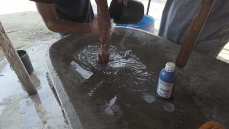 man washing hands in a concrete basin with a wooden stick, clear water swirling