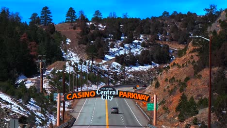 welcome to sign central city parkway idaho springs blackhawk colorado aerial drone highway road bridge snow blue sky sunny clouds forest power lines car driving gilpin county static shot