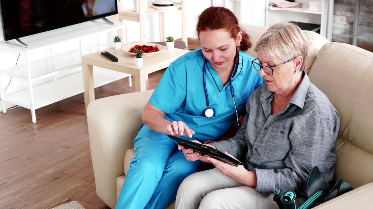 Female nuse helping senior elderly retired woman how to use her tablet computer