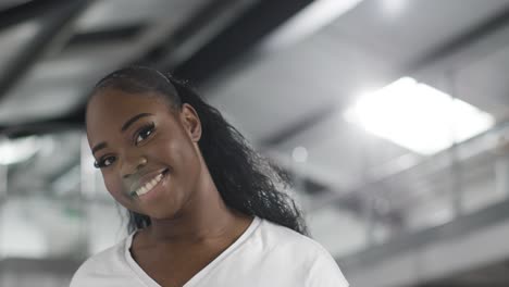 head and shoulders portrait of smiling young woman inside office building or warehouse looking at camera