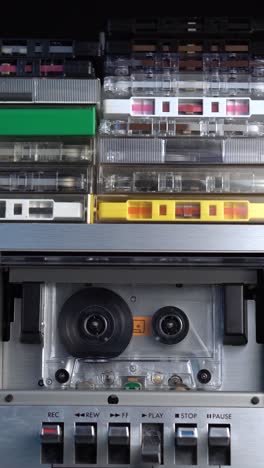 vertical view of hand placing audio cassette in deck with bunch of tapes on top and pressing play, close up