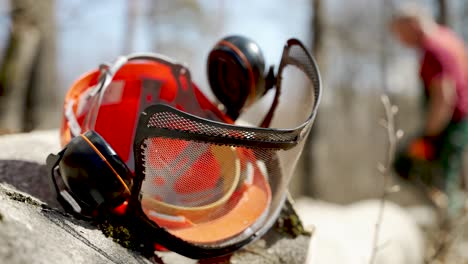 Close-Up-View-Of-Protective-Helmet-With-Visor-And-Ear-Protectors-Resting-On-Tree-Trunk-With-Bokeh-Background