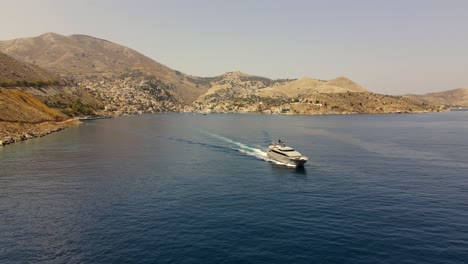 luxurious yacht leaves the city symi in greece during sunset, aerial pan right