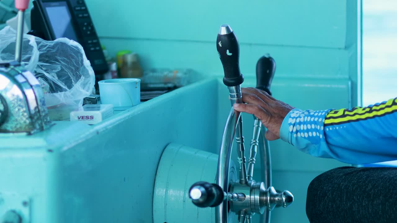 A captain skillfully maneuvers a fishing boat's helm in Phuket, Thailand. Bright lighting and close-up focus highlight the action