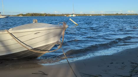 the bow of a boat tied up on a bank, bobbing up and down in the waves on the beach.