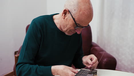 elderly man patiently trying to fix the strings of his guitar