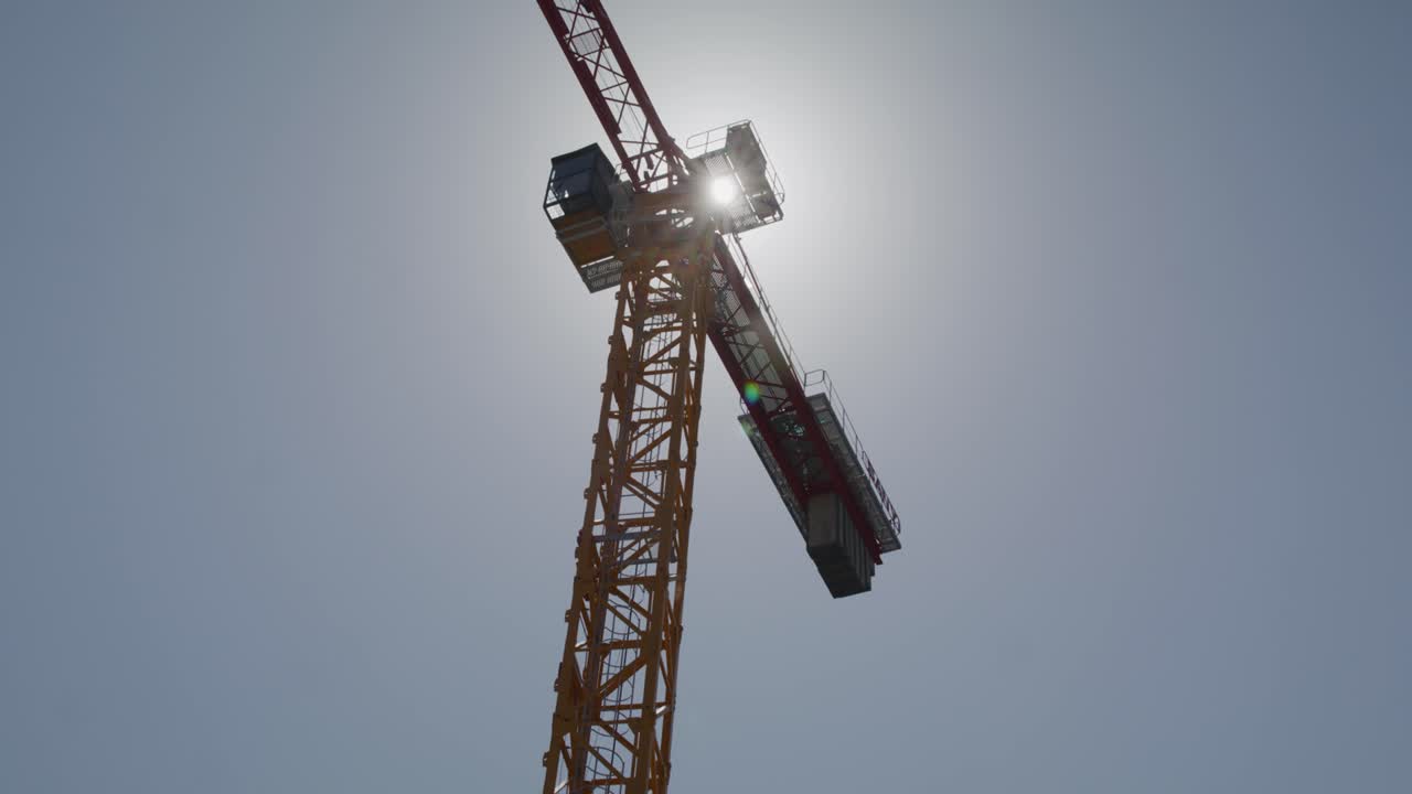 A majestic shot of a tower crane silhouetted against a bright sky, capturing the grandeur of this essential piece of machinery in the construction industry. The sun shines behind the crane