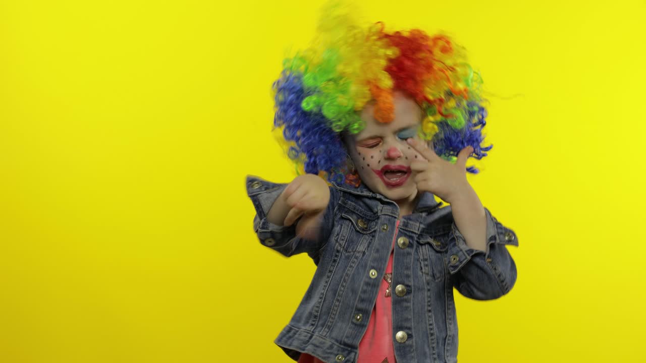 una niña payasa con una peluca colorida haciendo caras tontas. divirtiéndose, sonriendo, bailando. halloween